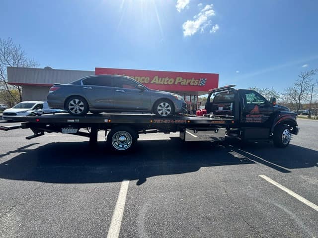 Gray sedan loaded on the Silverback flatbed outside an auto parts store