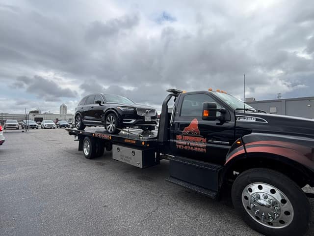 Dark SUV towed on the Silverback flatbed under a cloudy sky